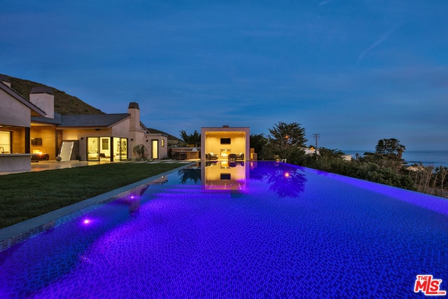 pool at dusk with a patio area and a yard