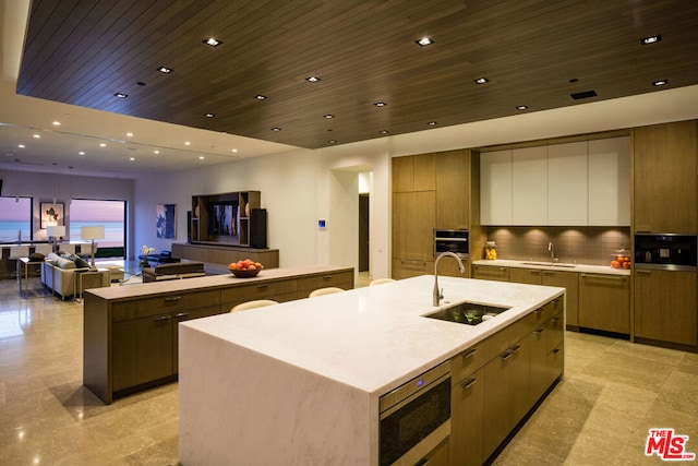 kitchen with stainless steel microwave, wood ceiling, sink, and a large island with sink