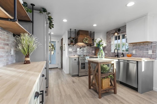 kitchen with appliances with stainless steel finishes, light wood-type flooring, custom range hood, and sink