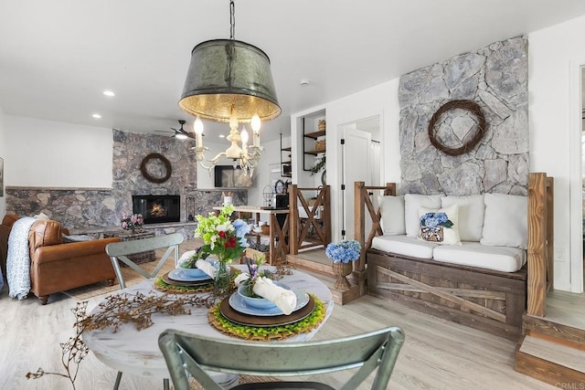 dining room featuring a stone fireplace, hardwood / wood-style floors, and ceiling fan with notable chandelier