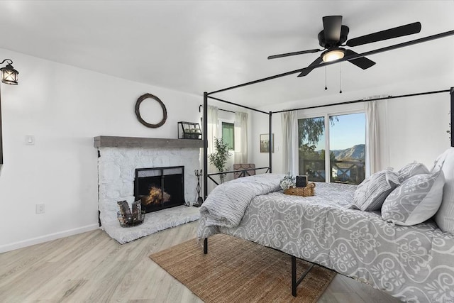 bedroom featuring a fireplace, light hardwood / wood-style flooring, and ceiling fan