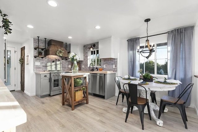 kitchen featuring hanging light fixtures, light hardwood / wood-style flooring, gray cabinets, custom range hood, and appliances with stainless steel finishes