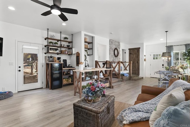 living room with ceiling fan with notable chandelier, light hardwood / wood-style floors, and built in features