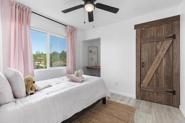 bedroom with a barn door, light hardwood / wood-style floors, and ceiling fan