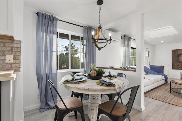 dining space with a chandelier, light hardwood / wood-style floors, a wall mounted AC, and a skylight