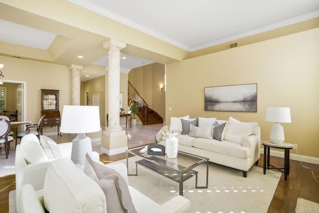 living room featuring wood finished floors, crown molding, baseboards, stairs, and ornate columns