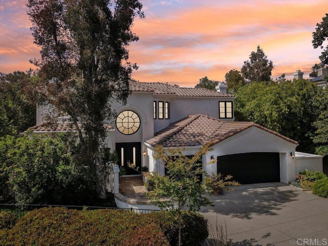 mediterranean / spanish-style home featuring concrete driveway, a tiled roof, a garage, and stucco siding