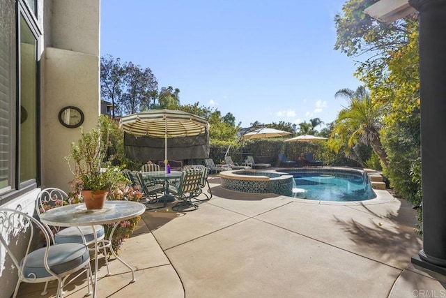 view of pool with fence, a pool with connected hot tub, outdoor dining space, and a patio area