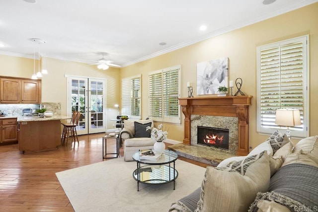 living area with light wood-style flooring, a high end fireplace, ceiling fan, french doors, and crown molding