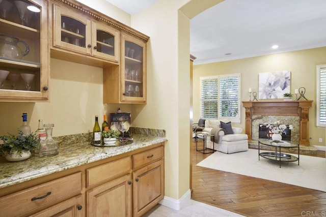 kitchen with a high end fireplace, glass insert cabinets, crown molding, and light stone counters