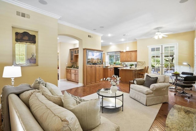 living area featuring arched walkways, visible vents, light wood-type flooring, and ornamental molding