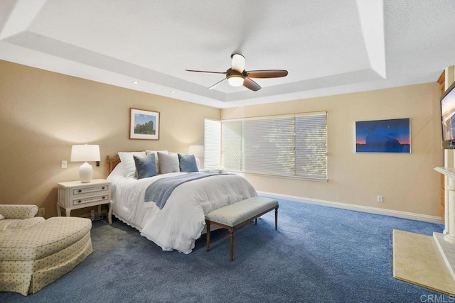 carpeted bedroom with a textured ceiling, a raised ceiling, baseboards, and ceiling fan