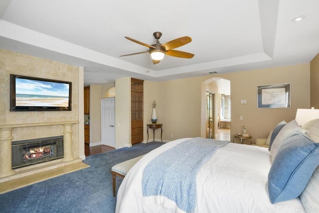 bedroom featuring connected bathroom, baseboards, a fireplace, arched walkways, and a raised ceiling