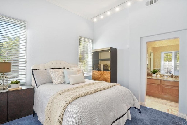 bedroom with visible vents, light colored carpet, rail lighting, ensuite bath, and a sink