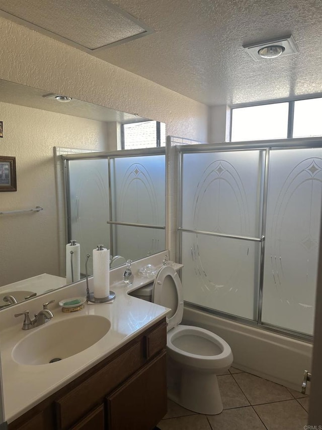 full bathroom featuring vanity, shower / bath combination with glass door, tile patterned floors, toilet, and a textured ceiling