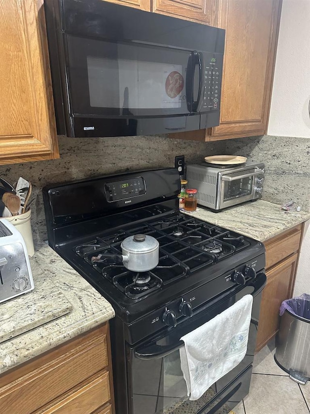 kitchen featuring light tile patterned flooring, light stone countertops, and black appliances