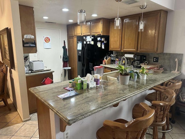 kitchen with kitchen peninsula, black fridge, stone counters, and light tile patterned floors