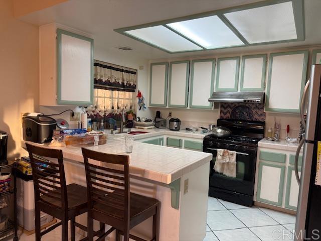 kitchen with black gas range oven, sink, stainless steel fridge, a kitchen breakfast bar, and kitchen peninsula