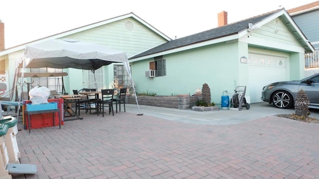 back of house with stucco siding, a chimney, a garage, and outdoor dining space