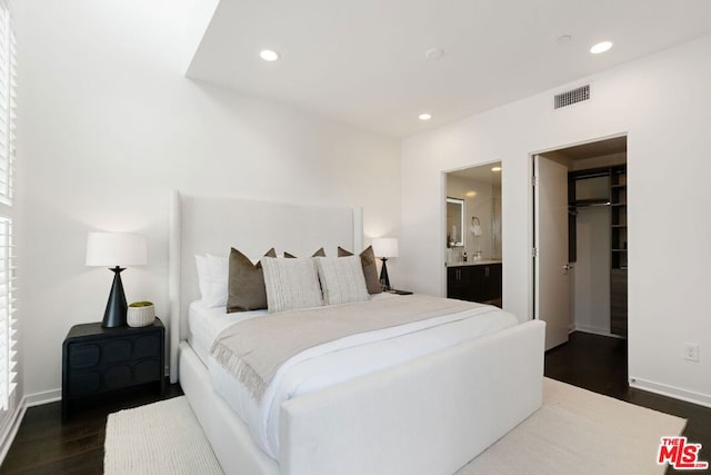 bedroom with a closet, a spacious closet, ensuite bath, and dark wood-type flooring