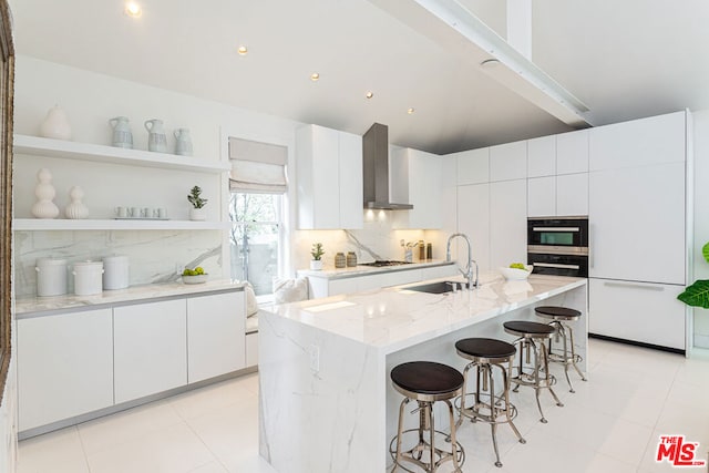 kitchen featuring a kitchen island with sink, oven, sink, wall chimney exhaust hood, and white cabinetry