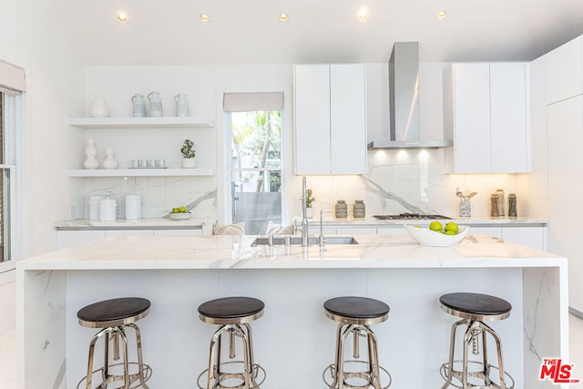 kitchen featuring wall chimney exhaust hood, a kitchen bar, and white cabinetry