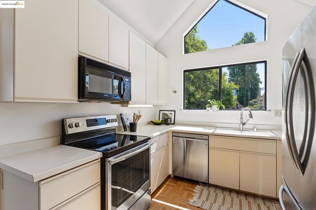 kitchen featuring sink, light parquet floors, stainless steel appliances, and vaulted ceiling