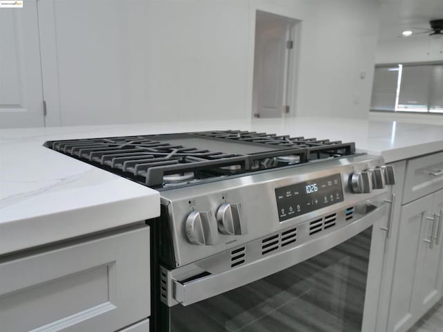 interior details featuring white cabinetry, light stone counters, and high end range