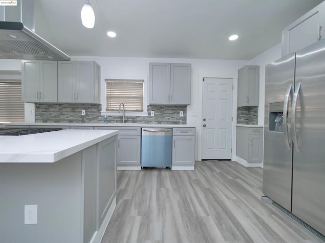 kitchen featuring appliances with stainless steel finishes, sink, wall chimney range hood, gray cabinets, and hanging light fixtures