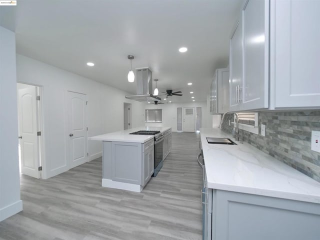 kitchen with pendant lighting, sink, stainless steel gas range, island range hood, and white cabinetry