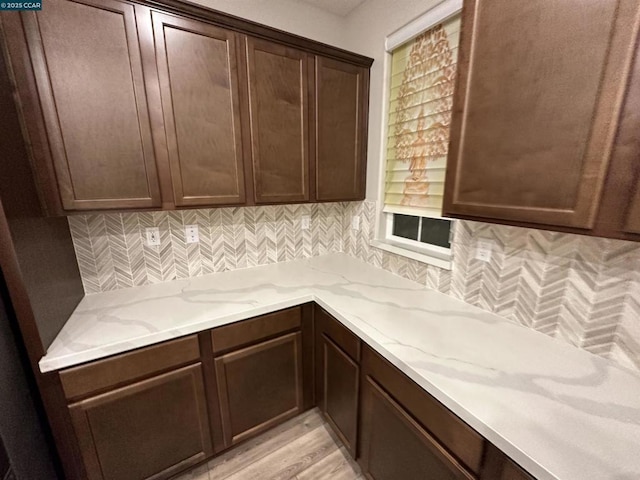 kitchen featuring light stone countertops, dark brown cabinets, light hardwood / wood-style floors, and decorative backsplash