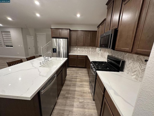 kitchen featuring stainless steel appliances, light stone counters, a center island with sink, and sink