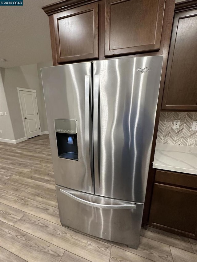 interior details featuring stainless steel fridge, backsplash, light stone counters, dark brown cabinetry, and light hardwood / wood-style flooring