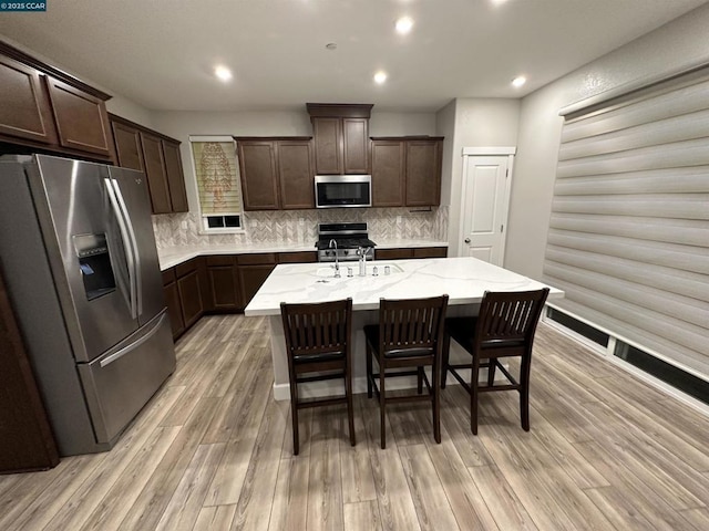 kitchen with appliances with stainless steel finishes, a kitchen breakfast bar, sink, a center island with sink, and light hardwood / wood-style flooring