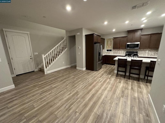 kitchen featuring dark brown cabinetry, stainless steel appliances, a kitchen breakfast bar, backsplash, and a kitchen island with sink