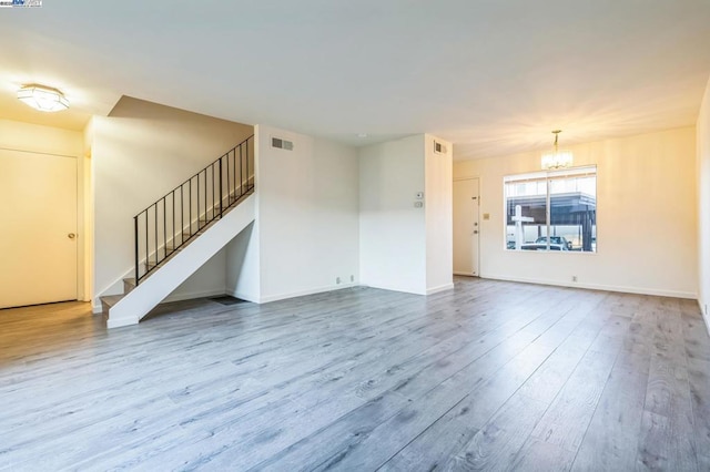 unfurnished living room featuring a notable chandelier and hardwood / wood-style flooring