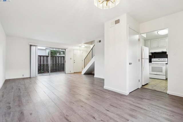 unfurnished living room featuring light wood-type flooring and a notable chandelier