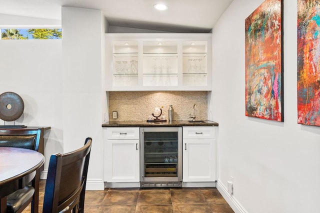 bar with beverage cooler, white cabinets, dark stone counters, and sink