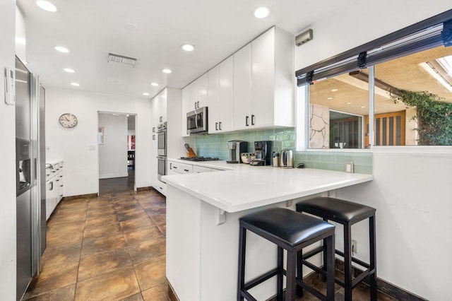 kitchen with backsplash, kitchen peninsula, a kitchen breakfast bar, stainless steel appliances, and white cabinets