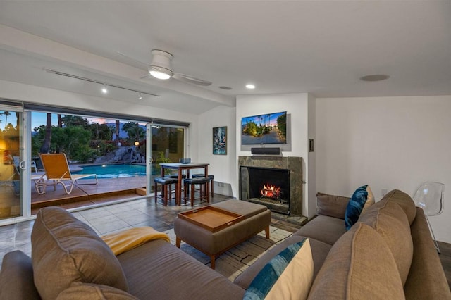 living room with vaulted ceiling, ceiling fan, rail lighting, and a stone fireplace