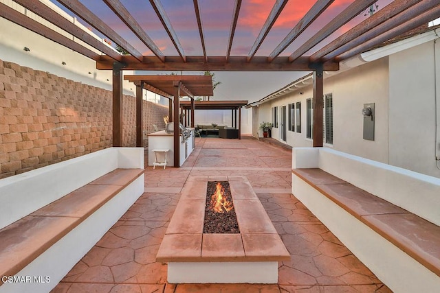 patio terrace at dusk featuring a pergola, area for grilling, and an outdoor fire pit