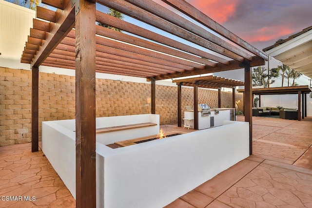 patio terrace at dusk with a pergola, an outdoor kitchen, and an outdoor living space with a fire pit