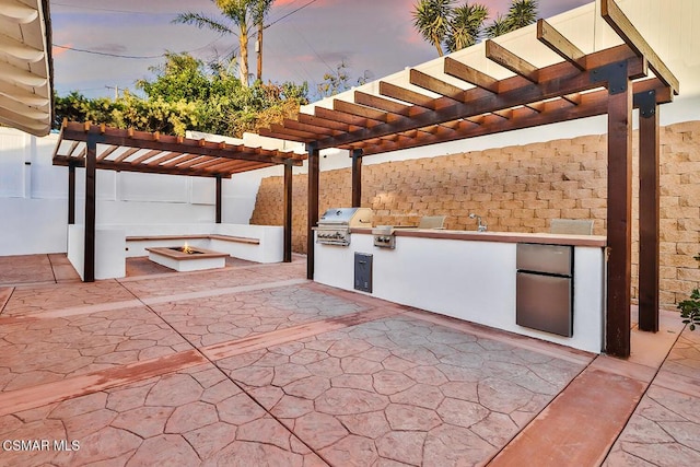 patio terrace at dusk featuring a pergola, a grill, and an outdoor kitchen