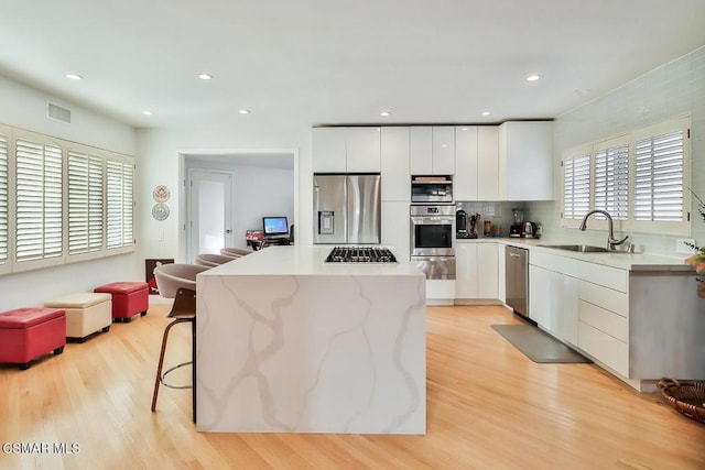 kitchen featuring appliances with stainless steel finishes, a kitchen breakfast bar, sink, light hardwood / wood-style floors, and white cabinetry