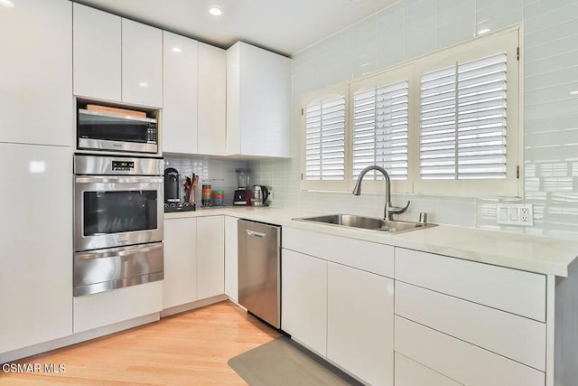 kitchen featuring white cabinetry, sink, decorative backsplash, appliances with stainless steel finishes, and light wood-type flooring