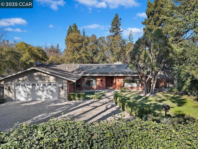 ranch-style house with solar panels, a garage, and a front lawn