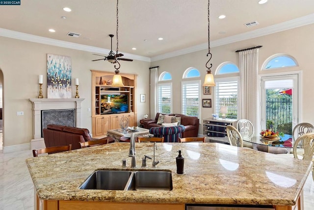 kitchen with a center island with sink, sink, light stone countertops, a fireplace, and decorative light fixtures