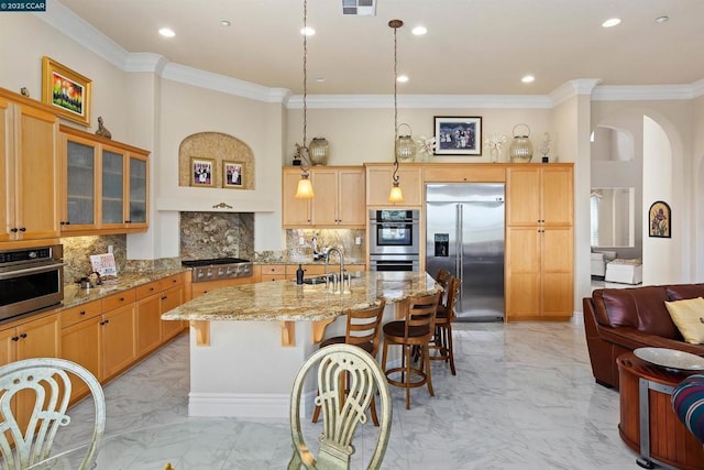 kitchen with light stone countertops, sink, an island with sink, decorative backsplash, and appliances with stainless steel finishes