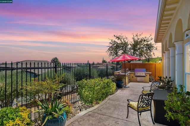 patio terrace at dusk featuring an outdoor kitchen and a grill