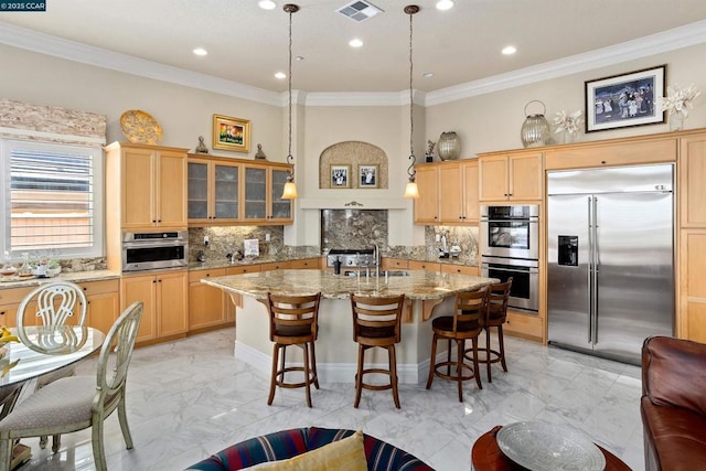 kitchen with light stone countertops, hanging light fixtures, tasteful backsplash, a center island with sink, and appliances with stainless steel finishes